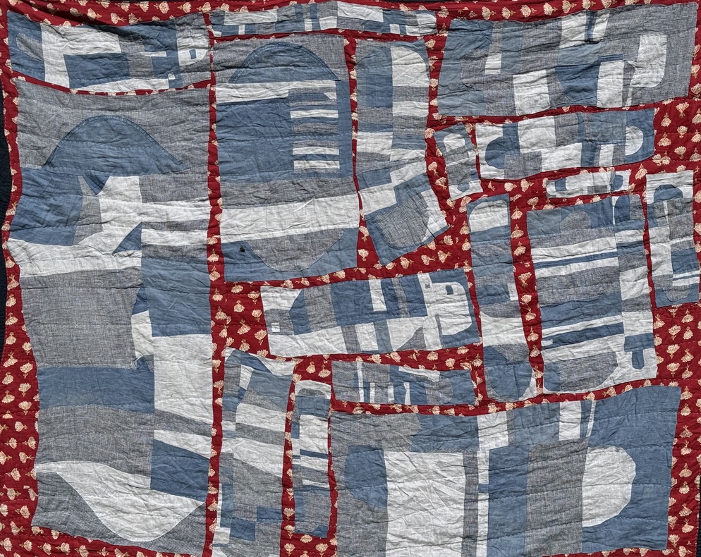 Abstract quilt with blue and white panels set in a red printed base fabric.