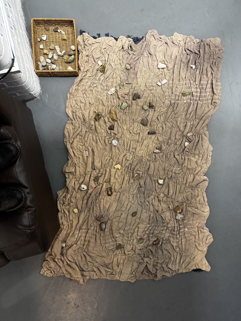 a stitched quilt on the ground with stones arranged on it
